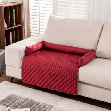 Alfombrilla impermeable para mascotas CloudSleep – alfombrilla acolchada roja y cojines sobre un sofá blanco, con lámpara y libros detrás