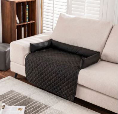 Alfombrilla impermeable para mascotas CloudSleep – alfombrilla acolchada negra sobre un sofá blanco, con un libro y un taburete cerca