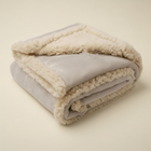 Couverture apaisante beige pliée, avec sa face lisse et sa doublure sherpa crème.