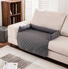 Alfombrilla impermeable para mascotas CloudSleep – alfombrilla acolchada gris sobre un sofá blanco junto a una ventana con cortina