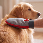 Grey and red grooming mitten brushing a dog’s coat, with the silicone palm facing the fur.