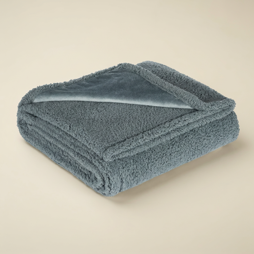 Couverture apaisante grise pliée, avec son tissu texturé et un coin lisse retourné.
