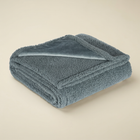 Couverture apaisante grise pliée, avec son tissu texturé et un coin lisse retourné.