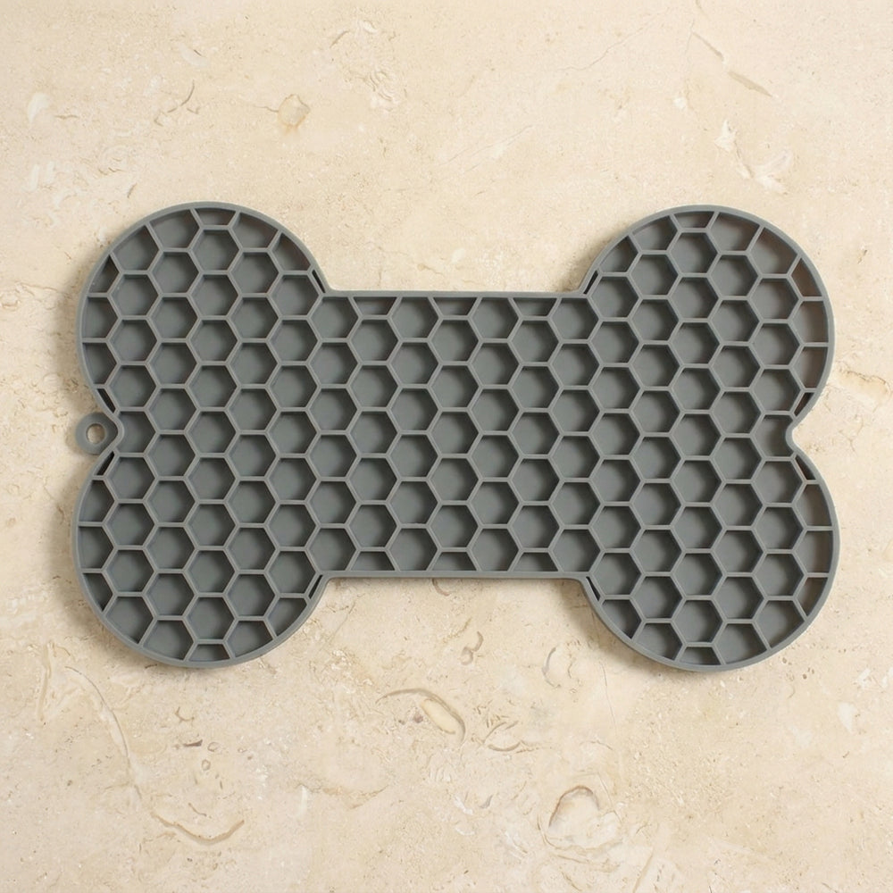 Alfombra gris para lamer en forma de hueso sobre una encimera de piedra clara.
