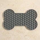 Alfombra gris para lamer en forma de hueso sobre una encimera de piedra clara.
