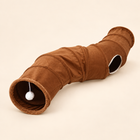 Brown curved polyester cat tunnel with side opening and hanging white pom-pom on a warm neutral background.