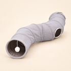 Grey curved polyester cat tunnel with side opening and hanging white pom-pom on a warm neutral background.